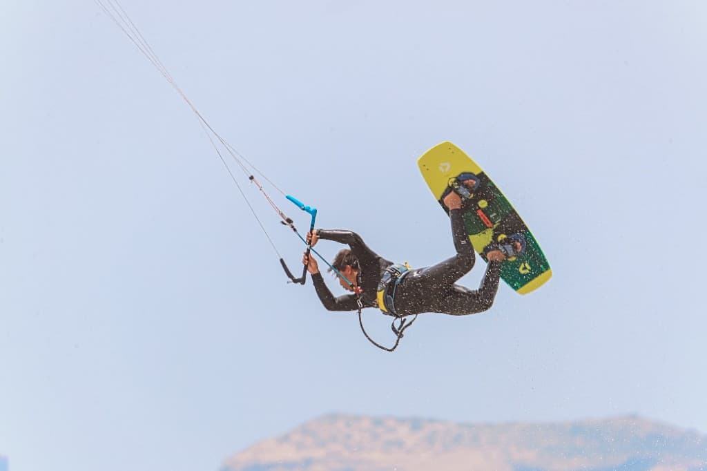 IKO kitesurf instructor airborne in a freestyle jump off Essaouira — twin-tip board, harness, and kite lines against a bright sky