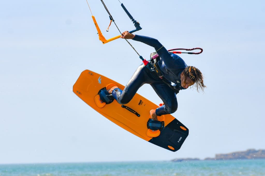 Kitesurfer high jump with an orange twin-tip board off Essaouira — harness, control bar, and pale Atlantic sky
