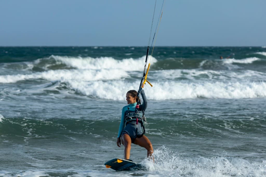 Smiling kitesurfer riding a twin-tip over choppy Atlantic waves off Essaouira — harness, control bar, and sea spray