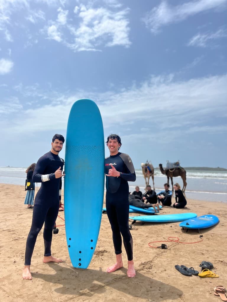 Surf students in wetsuits with a longboard on Essaouira’s sandy beach — Atlantic surf school, Morocco.